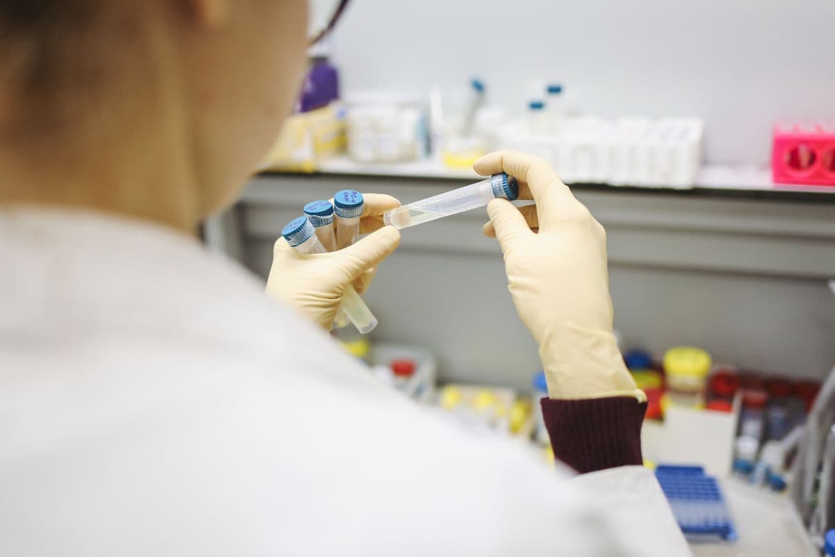 A gloved hand holds up a sample vial in a laboratory